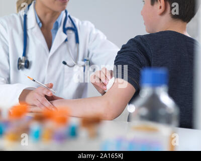 Medico donna dando un ragazzo di una vaccinazione di routine nella clinica Foto Stock