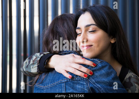 Giovani amici di sesso femminile con gli occhi chiusi abbracciando insieme in corrispondenza della parete Foto Stock