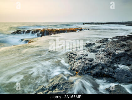 Spruzzi delle onde sulle rocce vulcaniche nella baia di Kealakekua contro sky durante il tramonto Foto Stock