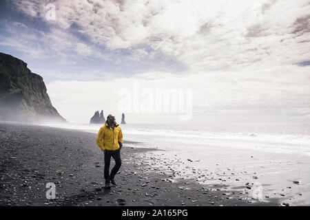 Uomo maturo a camminare su una spiaggia di lava in Islanda Foto Stock