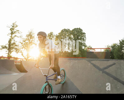 Felice giovane uomo equitazione biciclette BMX a skatepark al tramonto Foto Stock