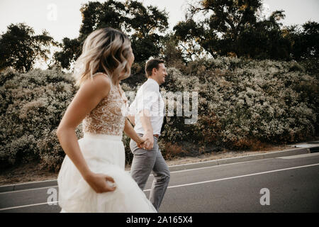 Sposa e lo sposo camminando mano nella mano su una strada di campagna Foto Stock