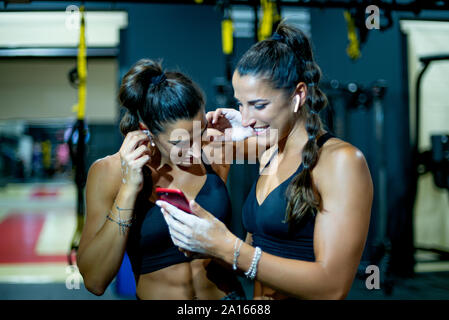 Twin felice sorelle in palestra con lo smartphone e le cuffie Foto Stock