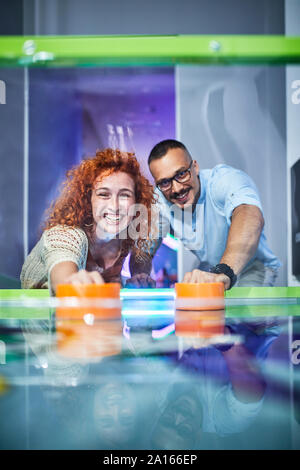 Coppia felice giocare air hockey e divertirsi in una sala giochi Foto Stock