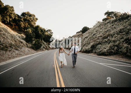 Sposa e lo sposo camminando mano nella mano su una strada di campagna Foto Stock