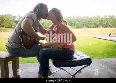 Uomo con guitar kissing Donna con bambina seduta sul suo giro Foto Stock
