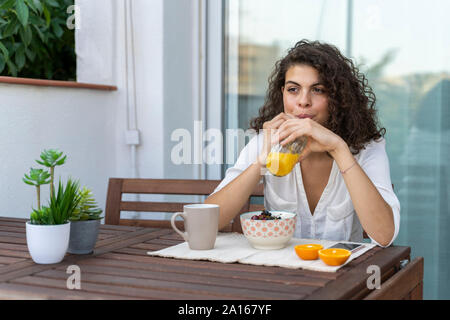 Giovane donna di bere succo di arancia sul balcone Foto Stock