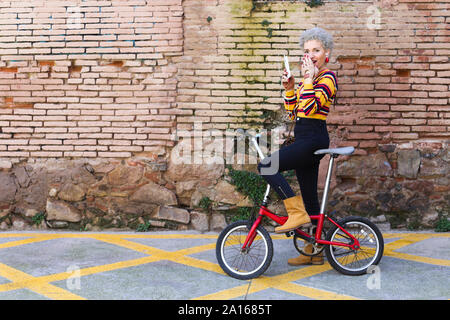 Moda donna matura con la bicicletta e smartphone su strada Foto Stock