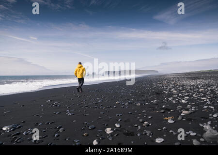 Uomo maturo a camminare su una spiaggia di lava in Islanda Foto Stock