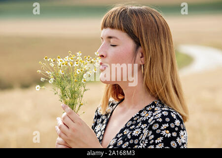 Giovane donna con gli occhi chiusi maleodoranti mazzetto di fiori di camomilla Foto Stock