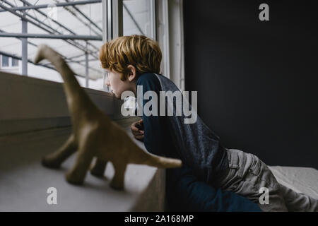 Triste ragazzo appoggiata sul davanzale guardando fuori della finestra di sera Foto Stock