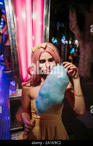 Ritratto di una giovane donna con cotone candy su un luna park di notte Foto Stock