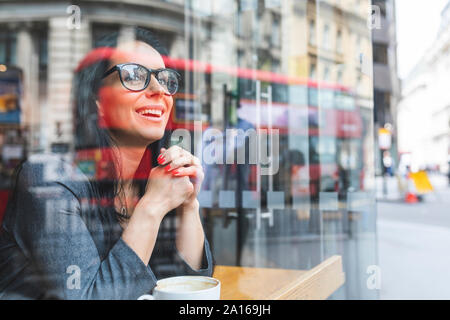 Donna sorridente dietro il vetro di finestra in un cafe Foto Stock