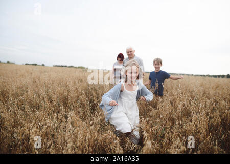 Ritratto di felice Ragazza che corre in un campo di avena mentre il fratello, nonna e nonno seguendo il suo Foto Stock
