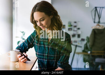 Giovane donna seduta in un coffee shop, utilizza lo smartphone Foto Stock