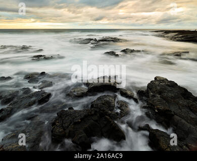 Le rocce vulcaniche immerso in acqua a Puuhonua O Honaunau National Historical Park contro il cielo nuvoloso durante il tramonto Foto Stock