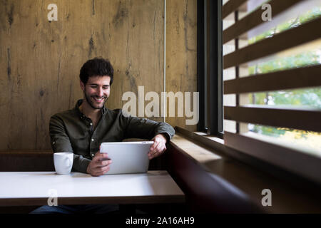 Ritratto di uomo sorridente con tavoletta digitale in un cafe Foto Stock