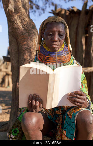 Tradizionale donna muhila, seduto sotto agli alberi, la lettura di un libro, Kehamba, Chibia, Angola Foto Stock