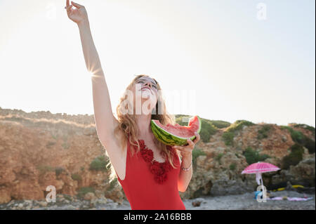 Spensierato giovane donna azienda fetta di cocomero sulla spiaggia Foto Stock