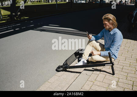 Giovane uomo con un telefono cellulare e e-scooter in città Foto Stock