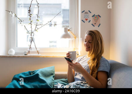 Giovane donna tramite telefono cellulare sul lettino a casa Foto Stock