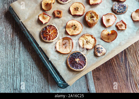 In casa delle fette di essiccato le arance e le mele sulla carta da forno e il vassoio da forno, disposizione diagonale, sullo sfondo di legno - angolo di visualizzazione, formato orizzontale Foto Stock