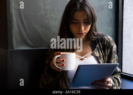Giovane donna seduta in cafe con la tazza di caffè e utilizzo di tablet Foto Stock