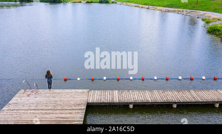 Vista aerea di una giovane triatleta femmina in piedi su un molo al lago Foto Stock