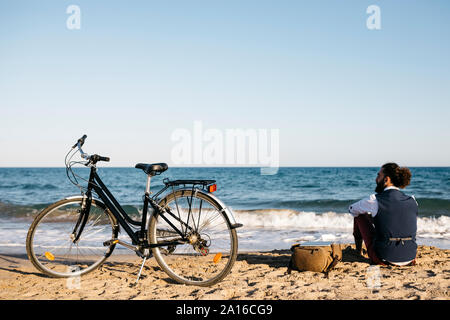 Ben vestito uomo con la sua moto seduto su una spiaggia Foto Stock