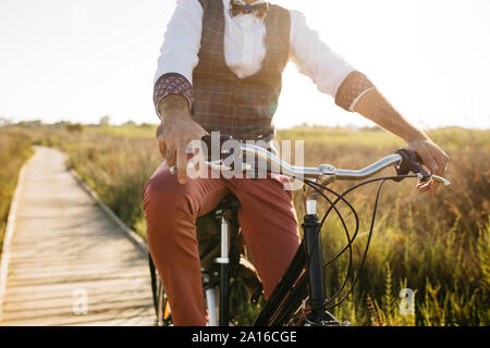 Ben vestito uomo con la sua bicicletta su una passerella di legno in campagna dopo il lavoro Foto Stock