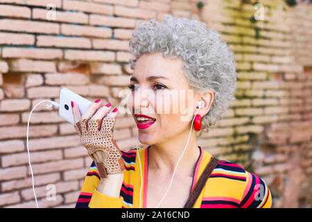 Ritratto di trafitto donna matura con auricolari telefonici sul telefono Foto Stock