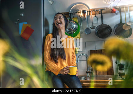 Ridendo giovane donna seduta sul banco di cucina a casa Foto Stock