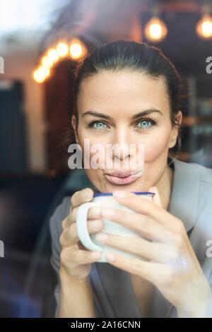 Ritratto di imprenditrice dietro il vetro di finestra in un bar a bere caffè Foto Stock