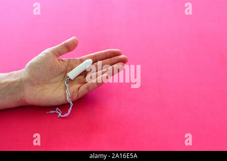 Tampone igienico per le donne in mano su sfondo rosa. Le mestruazioni o periodi concept Foto Stock