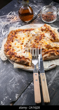 Quattro formaggi fette di pizza su un round tagliere al buio su un tavolo di legno. Close-up. Colpo verticale Foto Stock