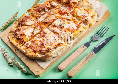Pizza Peperroni su un tagliere su uno sfondo verde. Close-up Foto Stock