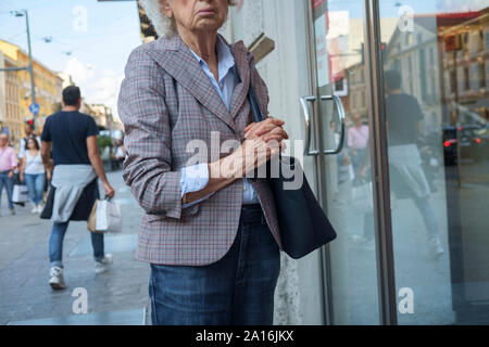 Donna anziana in fron t di una finestra di un negozio sul marciapiede in Milano Foto Stock