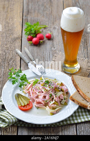 Sostanziosa bavarese insalata di salsiccia con strisce di formaggi, sottaceti e casale rustico pane serviti con una fresca birra di grano Foto Stock