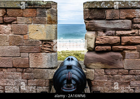 Un cannone puntando sul mare al castello di Bamburgh, Northumberland, Regno Unito Foto Stock