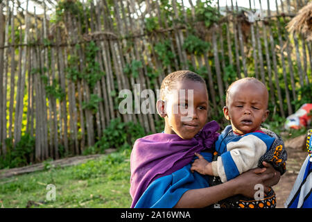 Masai bambini in abito tradizionale sono responsabili per i fratelli più giovani nel villaggio. Foto Stock