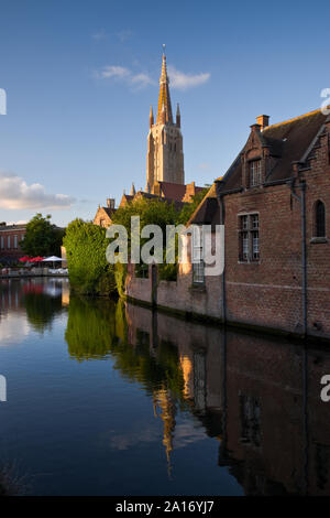 Il sole illumina il campanile della chiesa di Nostra Signora Bruges al tramonto, riflessa nel canale. Bruges, Belgio. Foto Stock