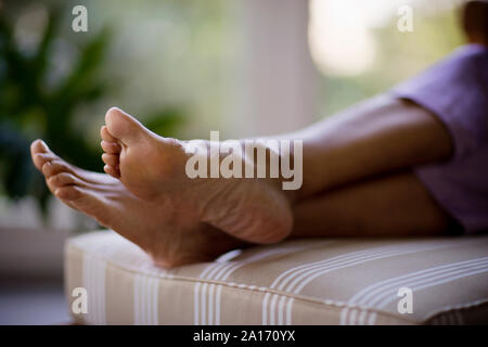 I piedi di una metà donna adulta rilassante su un ottomano. Foto Stock