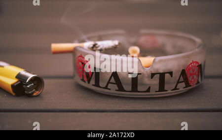 Sigaretta su un posacenere accanto a un accendino su un tavolo di legno Foto Stock