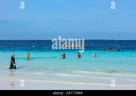 Kendwa, Zanzibar-March 4, 2019 : donna in abiti tradizionali con rete da pesca in mare presso la spiaggia di Kendwa Foto Stock