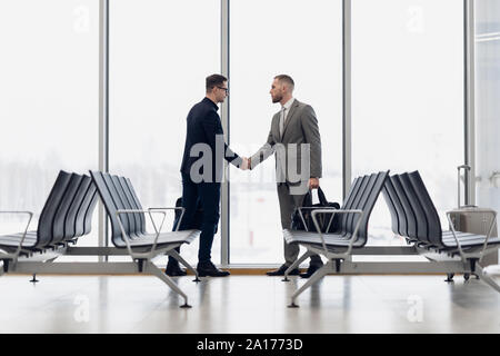 Lunghezza piena vista laterale di uomini di affari si stringono la mano nel terminal dell'aeroporto. Foto Stock