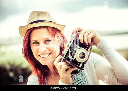 Ritratto di un bel sorriso i capelli rossi donna a scattare foto con una vecchia telecamera. trattamento vintage Foto Stock
