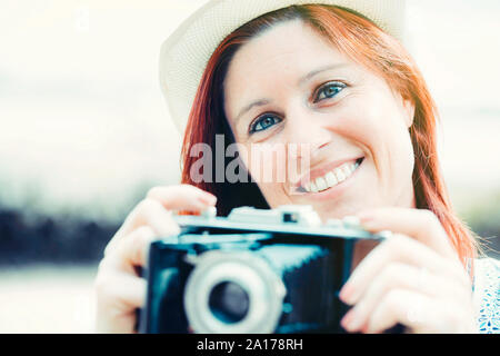 Ritratto di un bel sorriso i capelli rossi donna a scattare foto con una vecchia telecamera. trattamento vintage Foto Stock