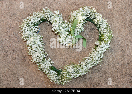 A forma di cuore bianco floreale con gli anelli di nozze legato in nastro verde Foto Stock