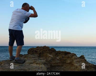 L'uomo guarda attraverso un telescopio al mare blu Foto Stock