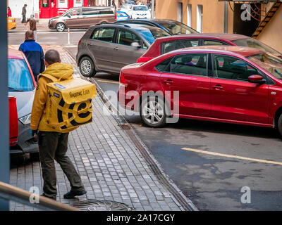 Mosca, Russia - 14 Settembre 2019: Servizi di corriere di cibo servizio di consegna in un uniforme di marca con un giallo zaino Yandex-Eda accanto a auto parcheggiate. Ther Foto Stock